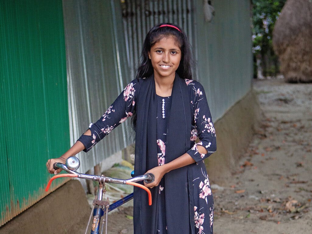 En flicka i mönstrad klänning som står med en cykel.