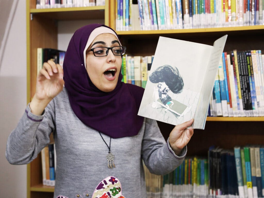 A woman reading loud from a childrens book at a library.