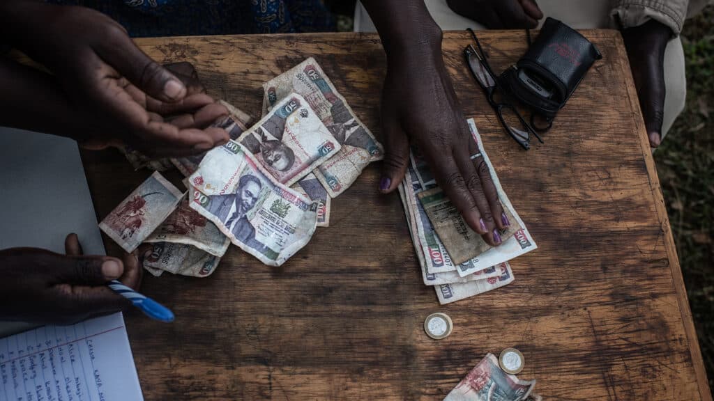 Sedlar och mynt ligger på ett bord, händer sträcker sig efter pengarna.