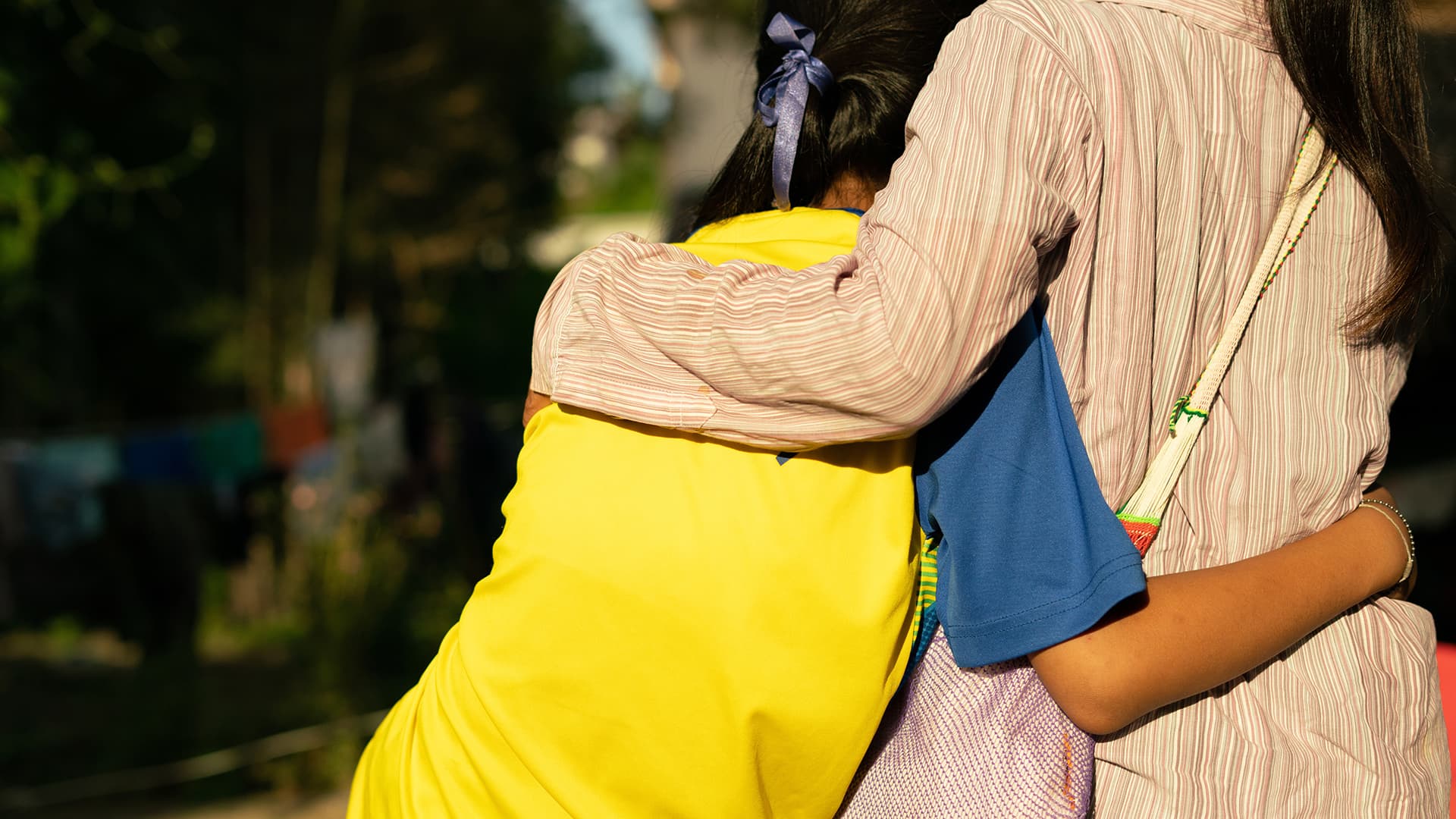 Vuxen håller om barn med ryggarna mot kameran.
