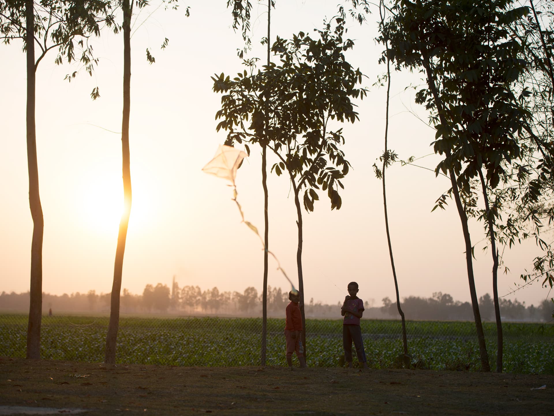 Två barn leker med en drake i solnedgången