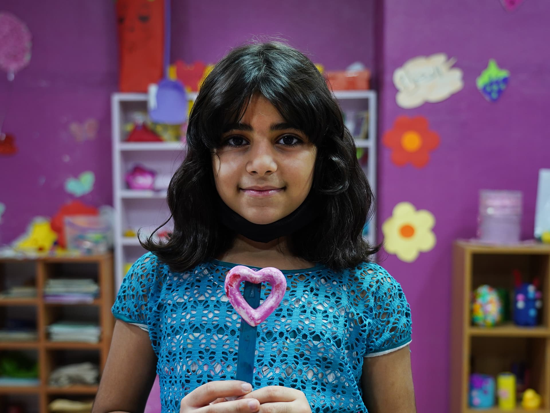 En flicka ser in i kameran. Hon håller upp ett hjärta i handen.