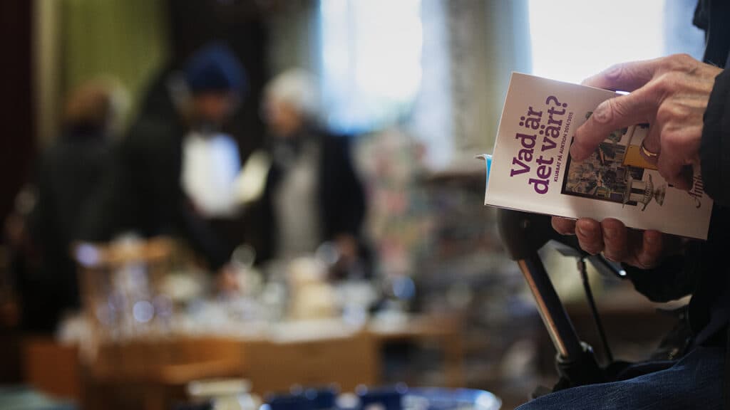 Bild på äldre persons hand som håller i en broschyr på en marknad