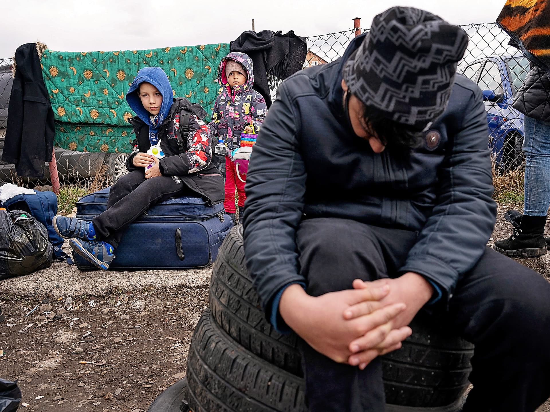 Två barn sitter på marken med framför ett stängsel där ett täcke hänger.