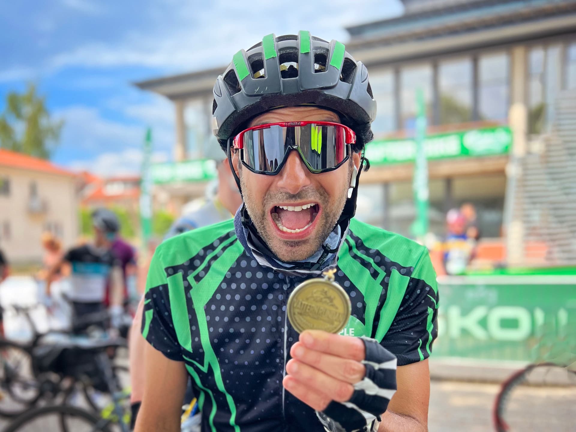 En bild av Stephan Wilson i solglasögon, cykelhjälm och med cykelhandskar som håller upp en medalj framför kameran.
