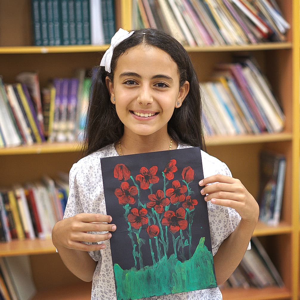 En flicka håller upp en teckning. På teckningen är det röda blommor mot svart bakgrund.