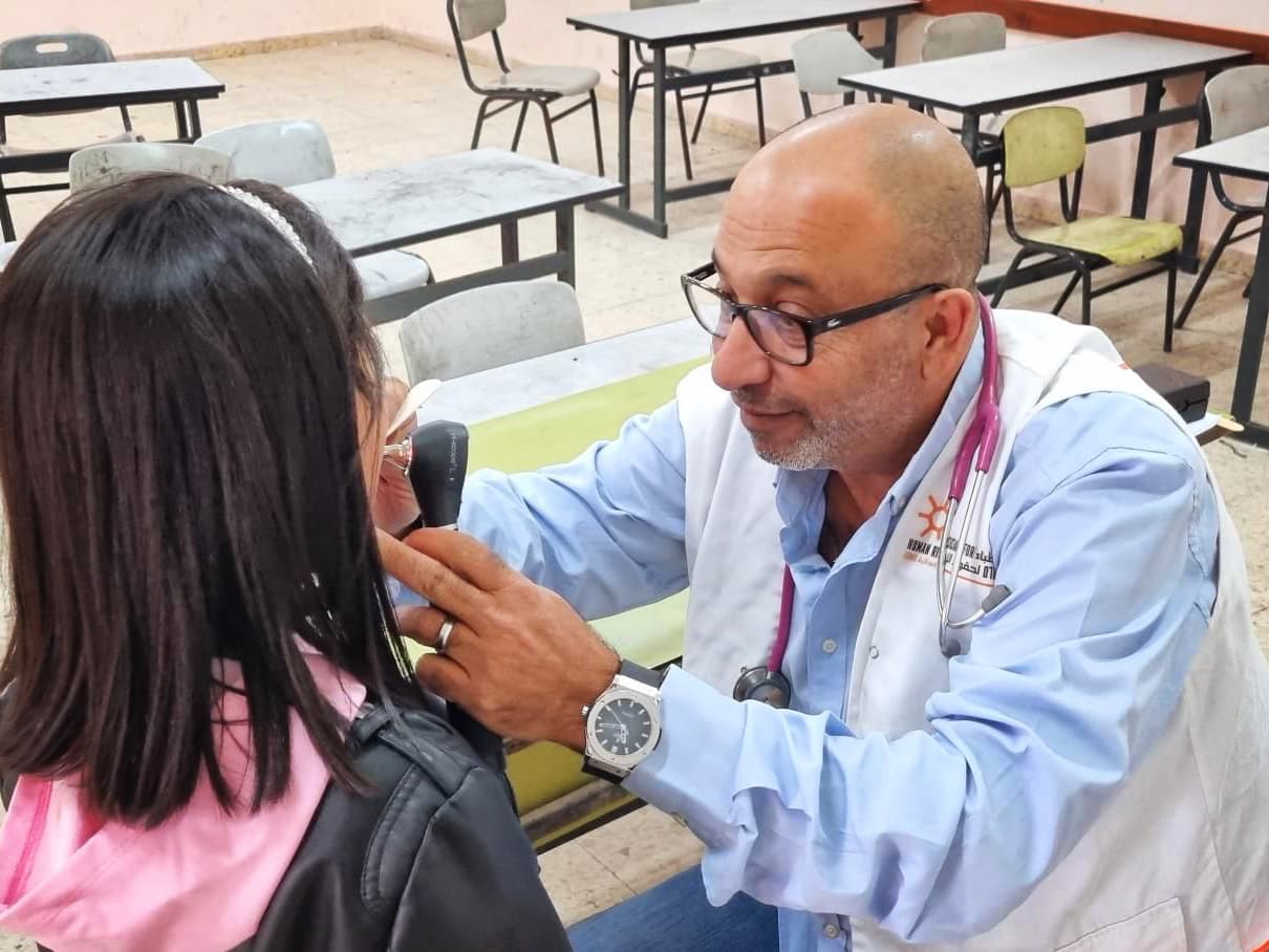 En man med vit väst och stetoskop runt halsen undersöker ett barn.