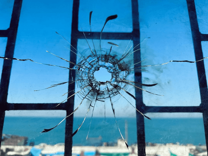 En fönsterruta med ett kulhål. Utsikten från fönstret är över havet.