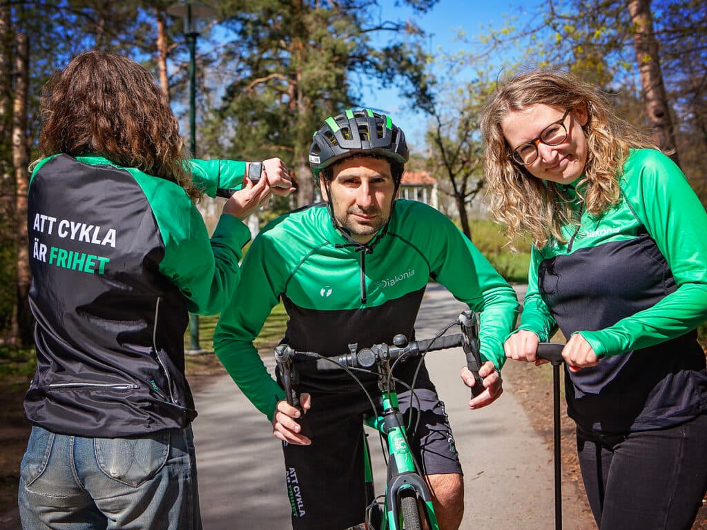 Tre personer i gröna cykelkläder och en cykel i mitten.