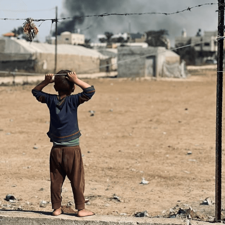 Ett barn står barfota med ryggen mot kameran och ser ut över ruiner.