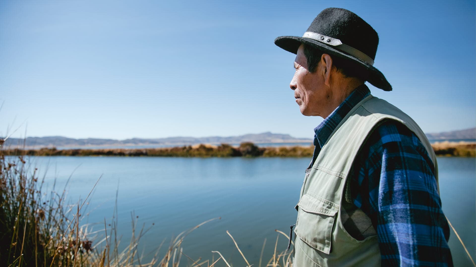 En man i hatt blickar ut över sjön.