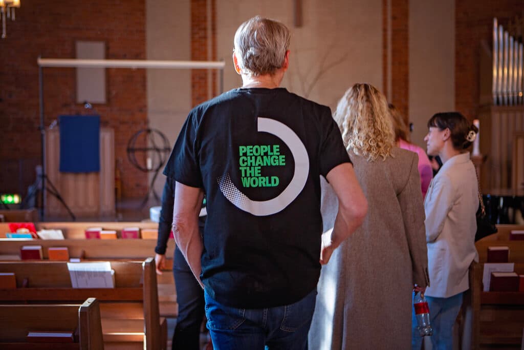 Bild tagen i en kyrka, i kyrkan står en man med Diakonias logga och trycket "People Change the World"