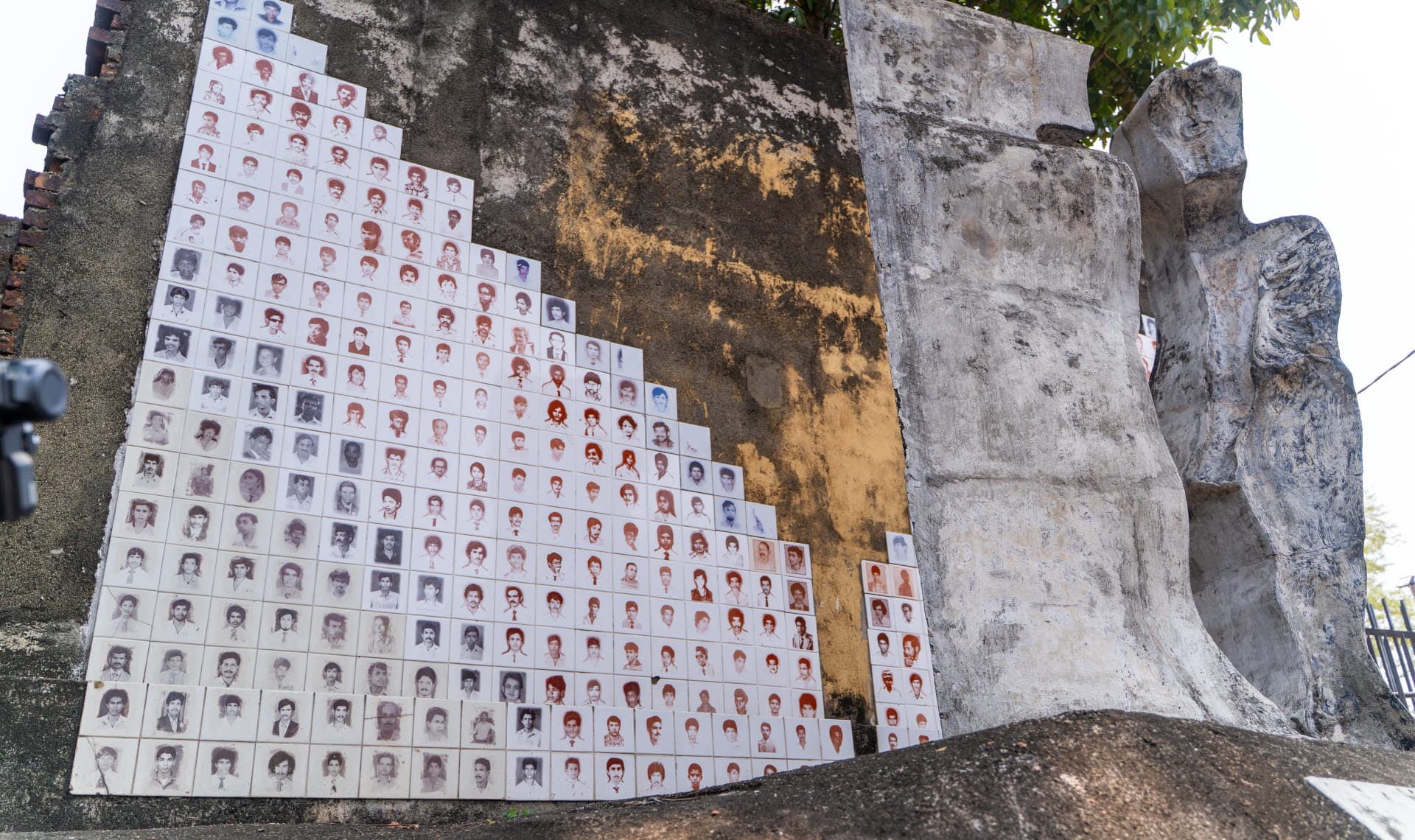 Monument vid en stenvägg, med foton på kakelplattor.