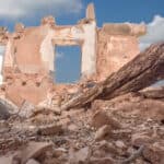 The rubble of a destroyed building and in the background a remains of a house wall.