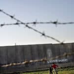 Two children play football in front of a concrete wall.