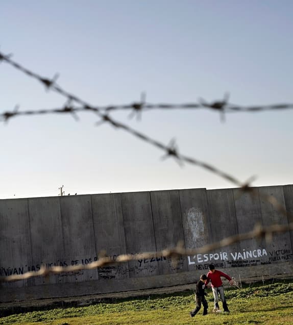 Two children play football in front of a concrete wall.