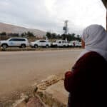 A woman watching United Nations vehicles, as part of a humanitarian convoy.