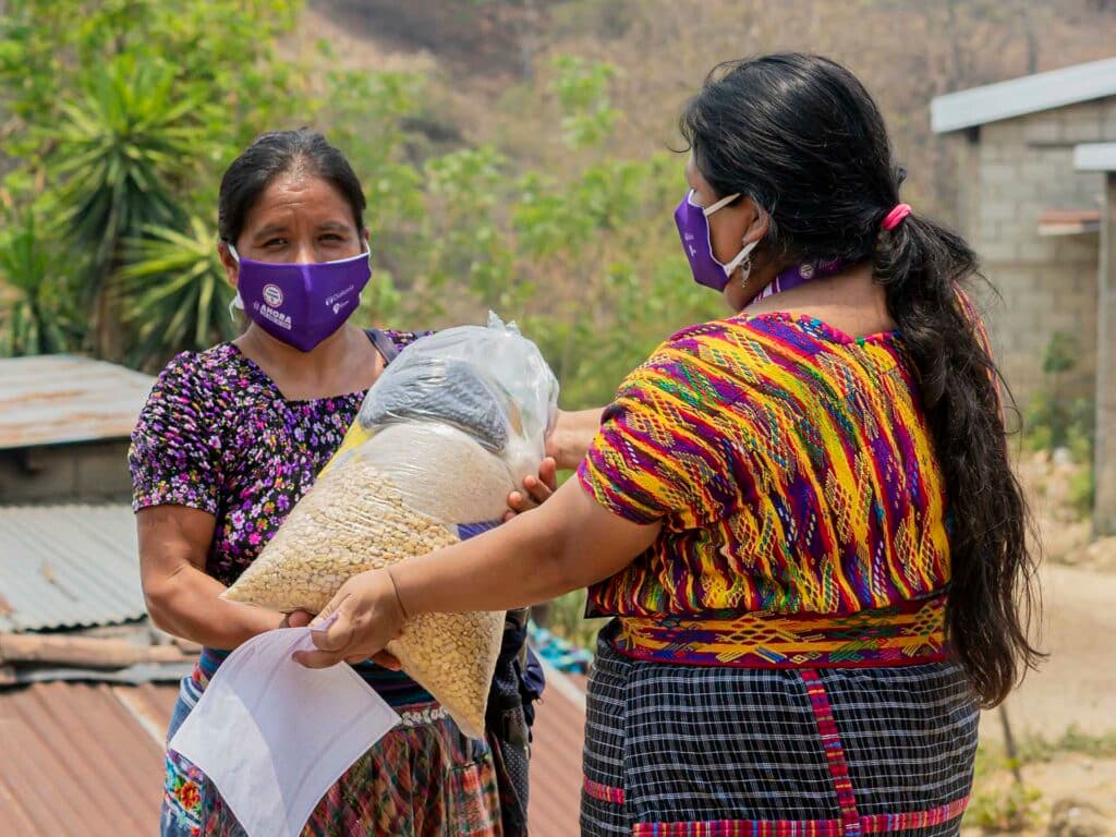 Dos mujeres con barbijos sosteniendo paquete de comida.