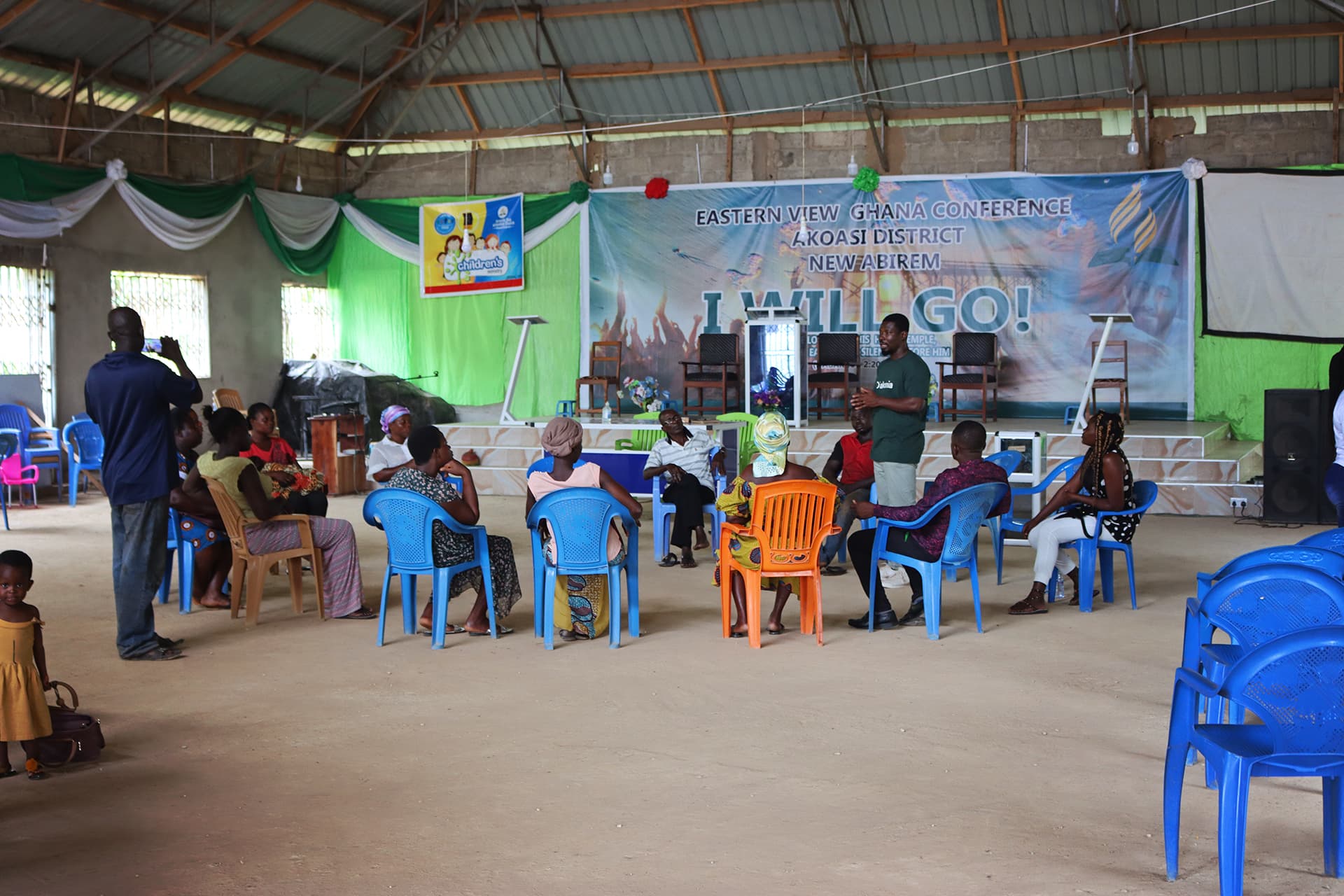 A group of people sitting in plastic chairs in a big meeting room.