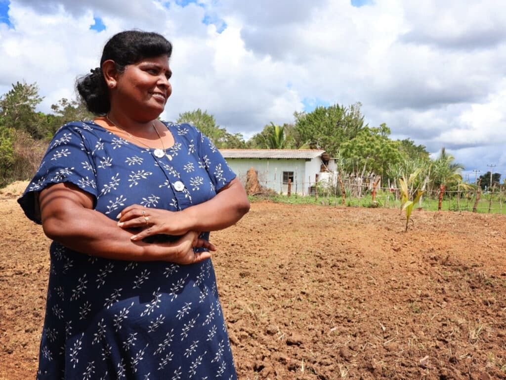 A darkhaired woman in a blue blouse stands in a field.