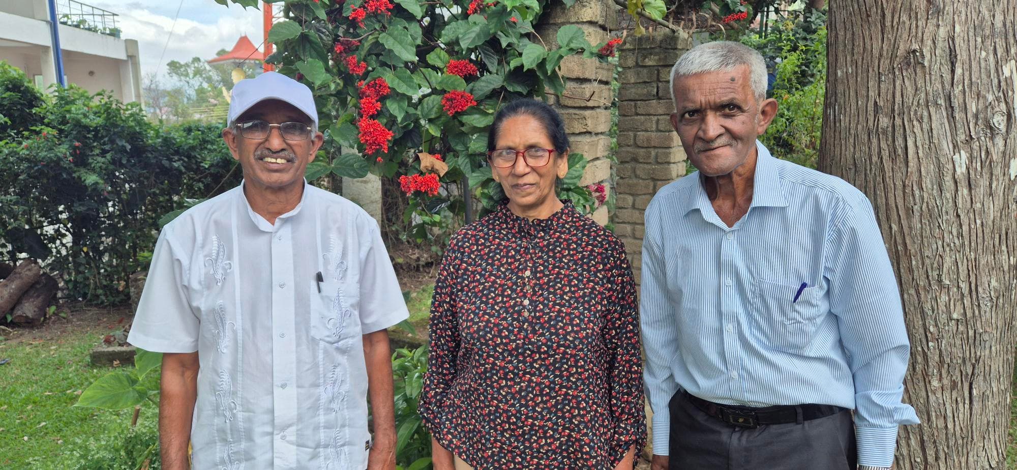 Three senior citizens from Sri Lanka standing in front of the open space with some trees behind - horizontal shot