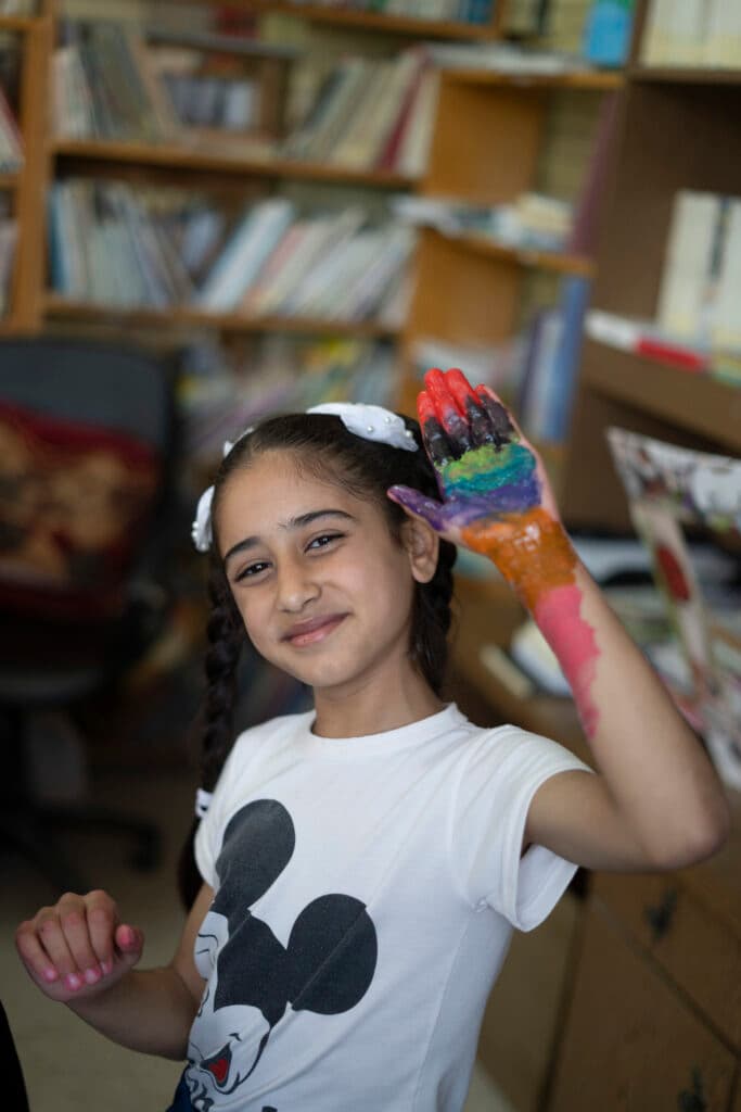 Flicka som håller upp sin hand som är målad i flera olika färger.