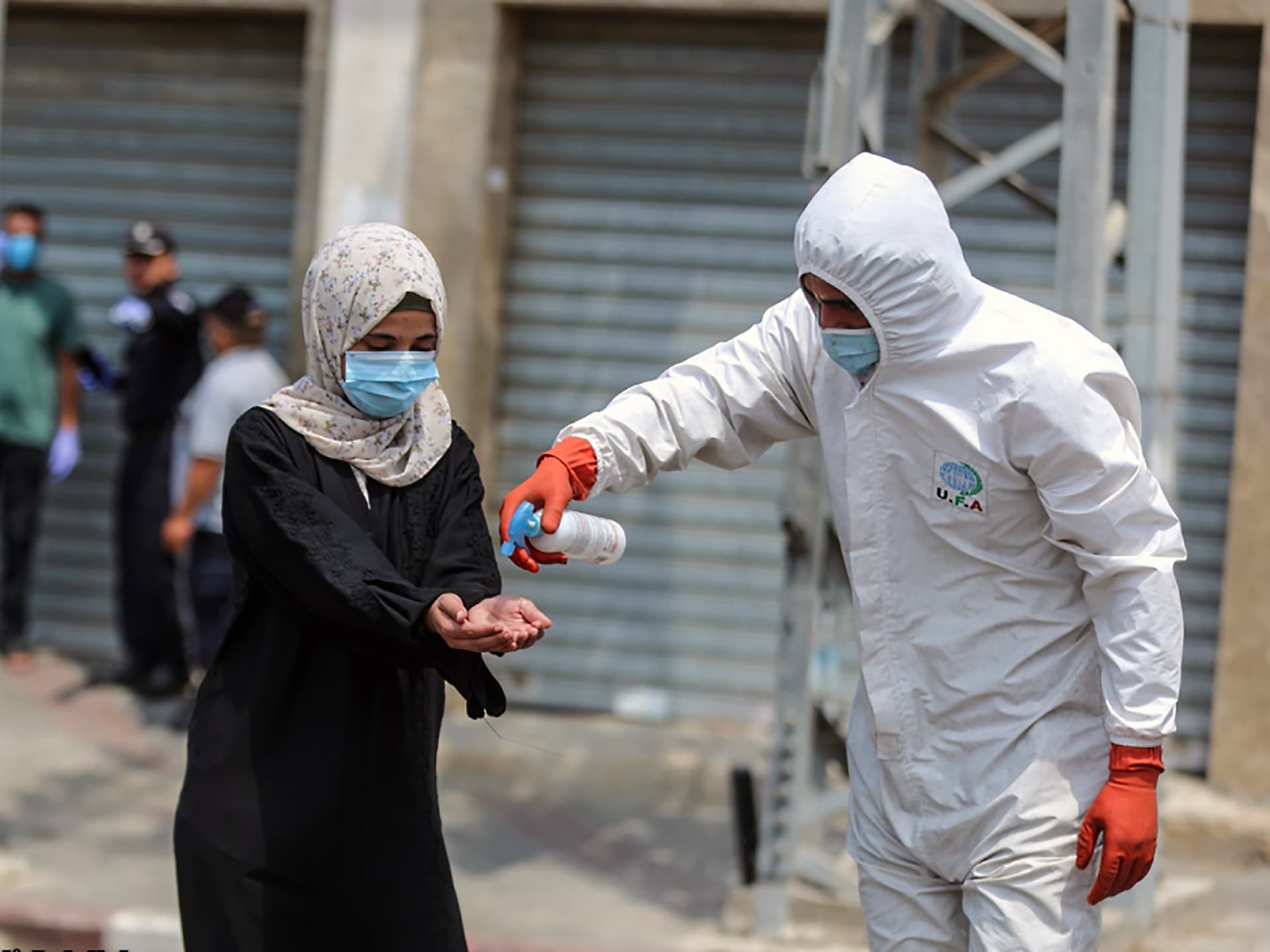 Foto: Ali Jaddalah Man i skyddskläder spritar kvinnas händer