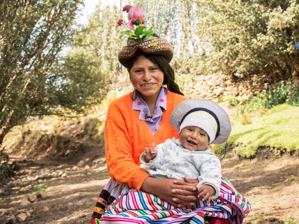 Foto: Laura Ardila En leende kvinna sitter i ett grönområde med en bebis i famnen.
