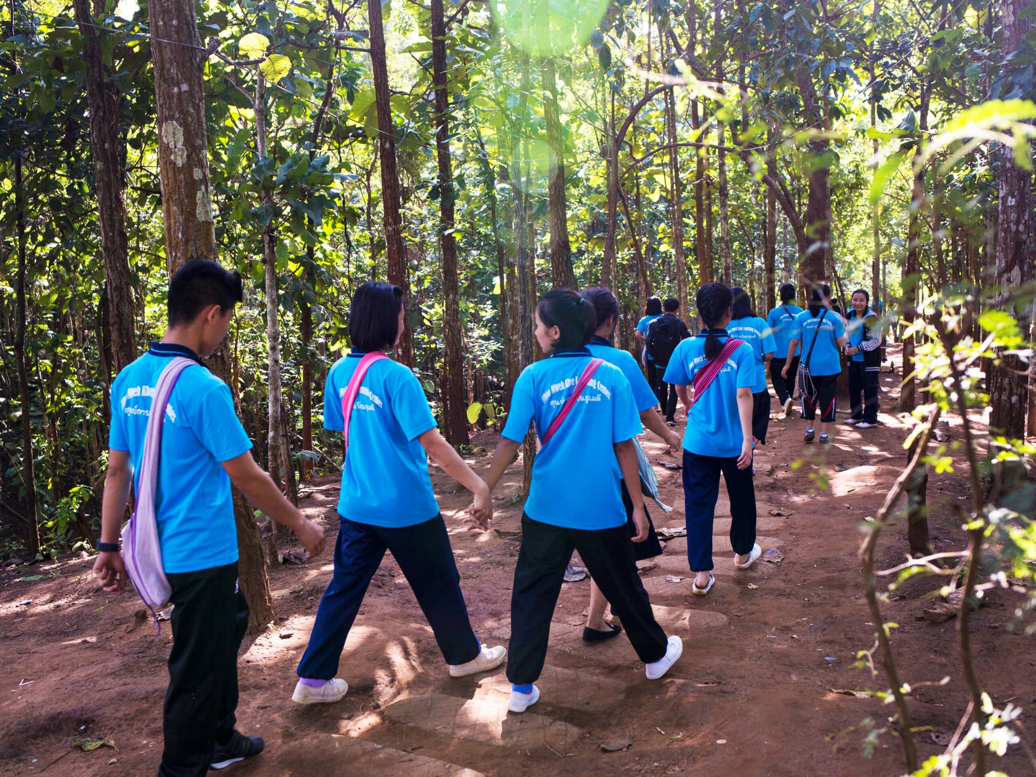 Foto: Biel-Calderon Flera människor i likadana ljusblåa t-shirts med text på ryggen går genom ett skogsområde, några håller varandra i handen.