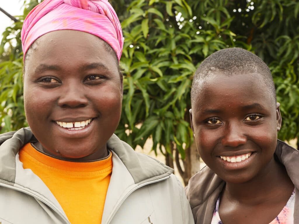 Foto: Diakonia Närbild av två leende ungdomar. Den ena har en rosa sjal på huvudet. Bakom dom syns gröna träd.