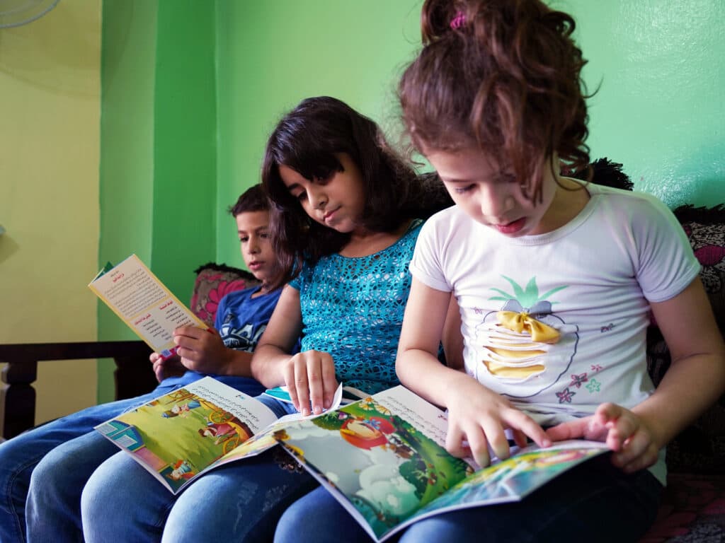 Foto: Adib Farhat Tre barn i en soffa tittar i barnböcker