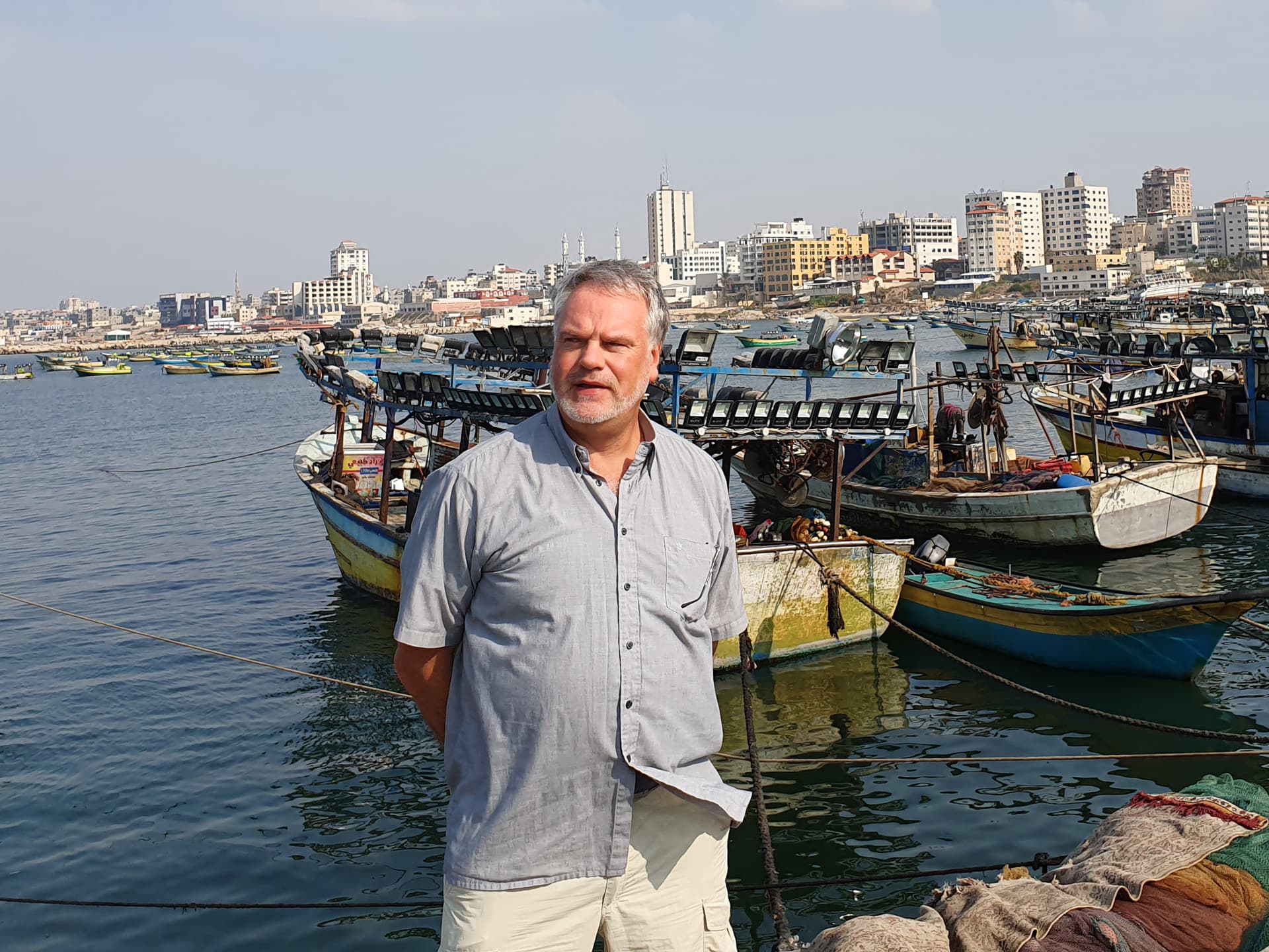 Foto: Diakonia En man på en kajkant med små fiskebåtar och stora hus i bakgrunden