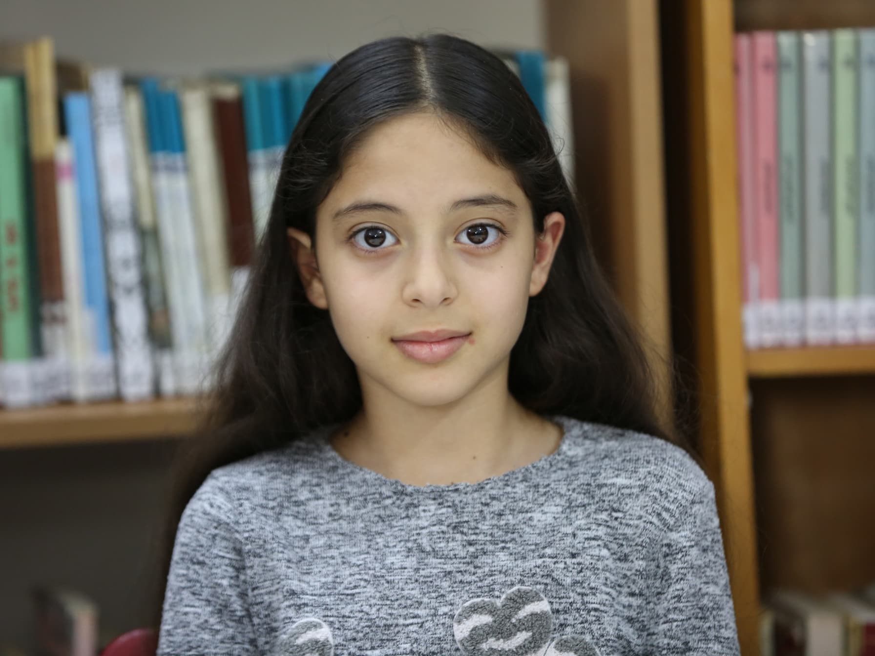 Foto: Abu Rahmah En flicka framför en bokhylla tittar in i kameran