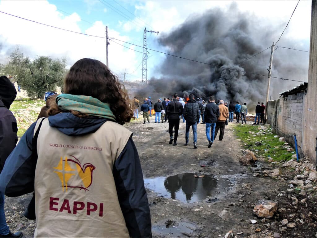 Foto: Hanna Lindh Ryggen på en kvinna med väst från följeslagarprogrammet och människor och en explosion längre bort