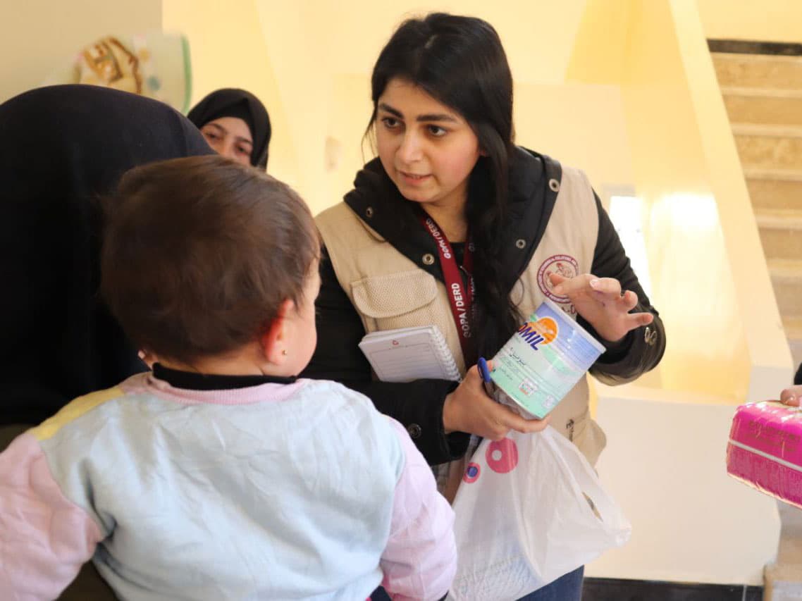 Foto: GOPA-DERD/Act alliance En hjälparbetare visar en burk barnmat för en mamma med barn.