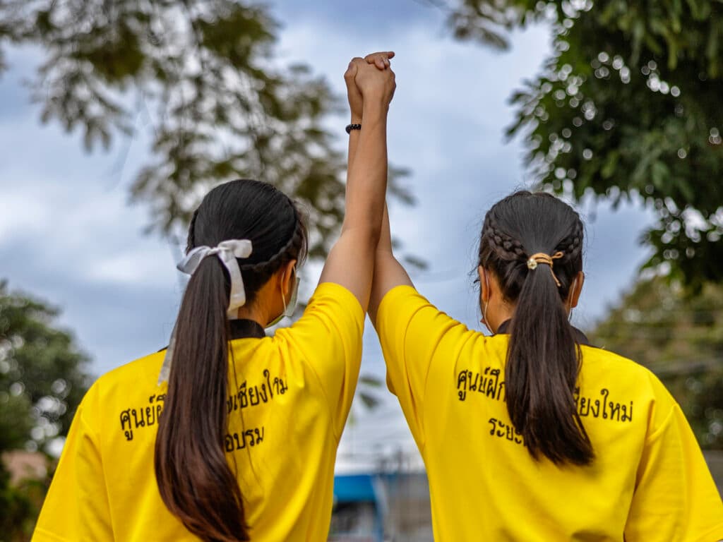 Foto: Jonas Gratzer Två unga kvinnor med ryggarna mot kameran håller varandra i händerna och sträcker upp armarna.