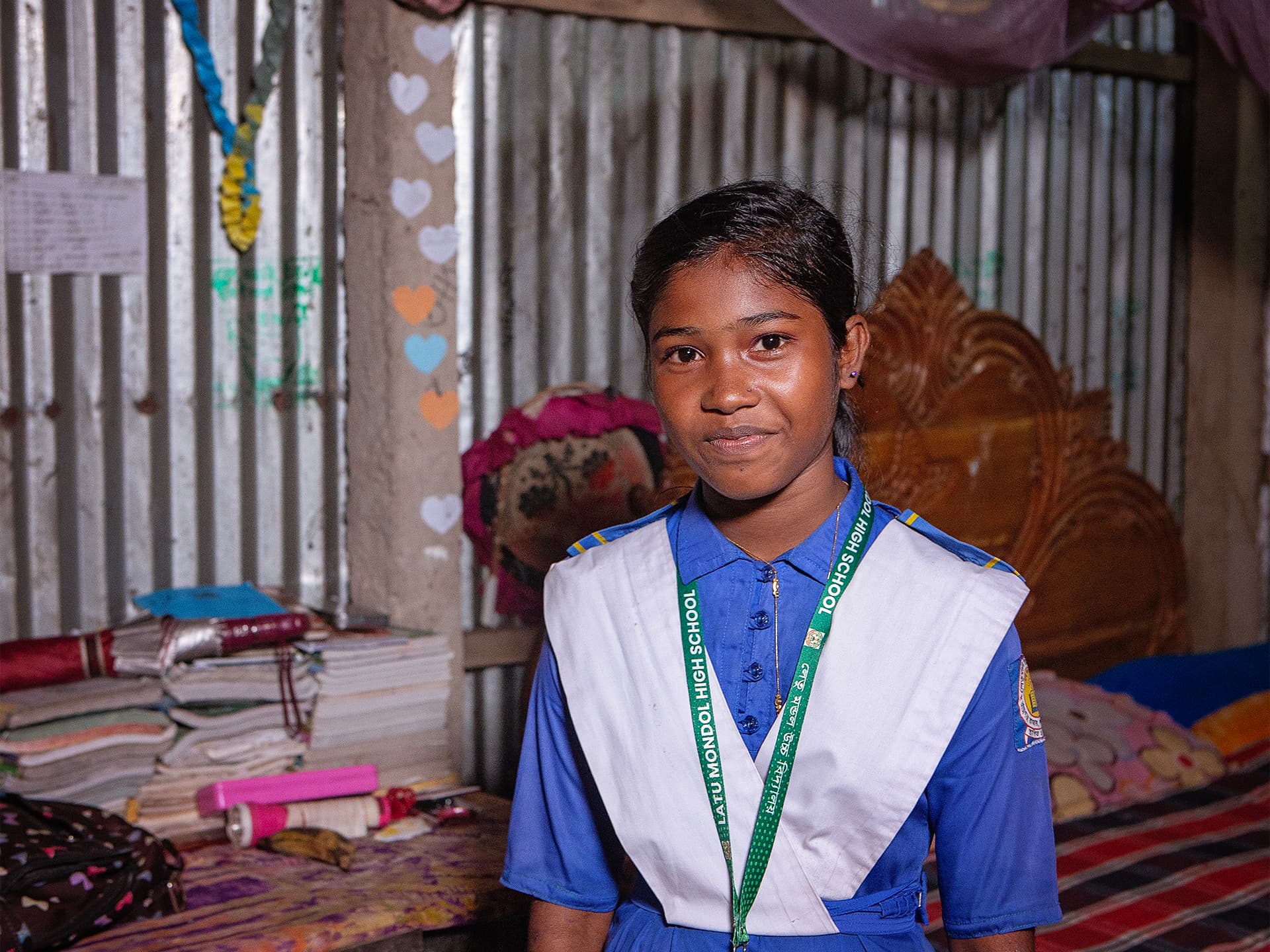 Foto: Diakonia En flicka i skoluniform står i ett rum med en säng och ett skrivbord bakom henne.