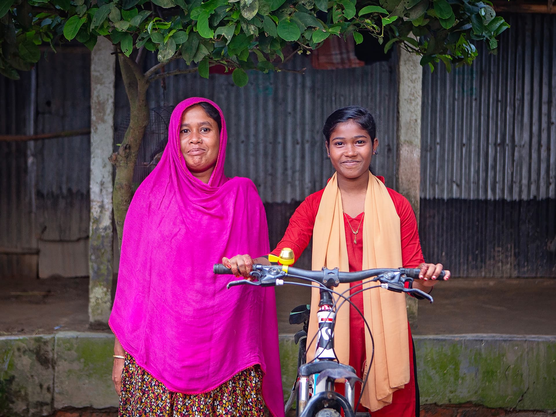 Foto: Diakonia En kvinna i rosa sjal bredvid en flicka i röd klänning med en cykel framför sig.