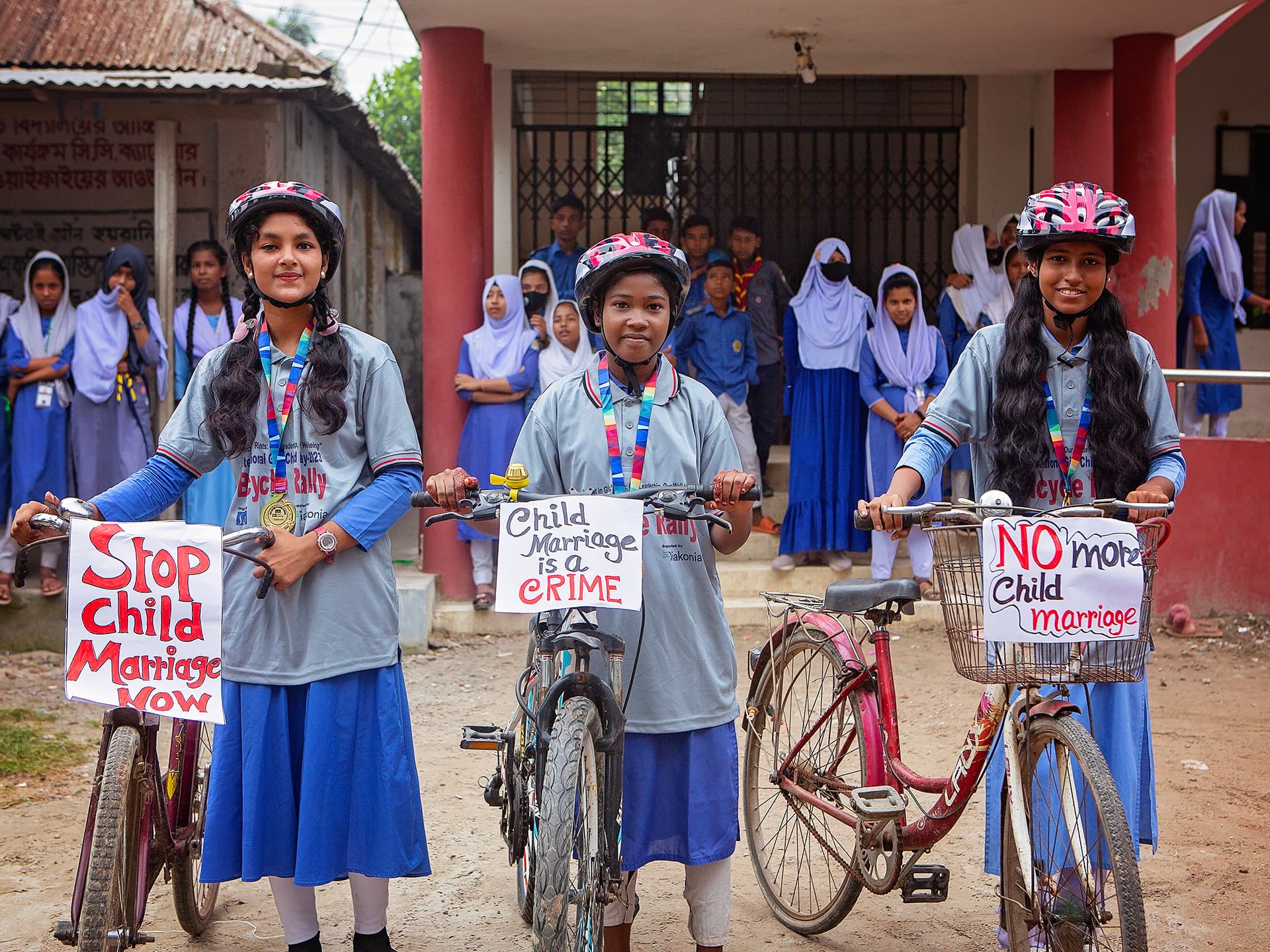Foto: Diakonia Tre flickor i likadana t-shorts tår med hjälmar framför en varsin cykel.