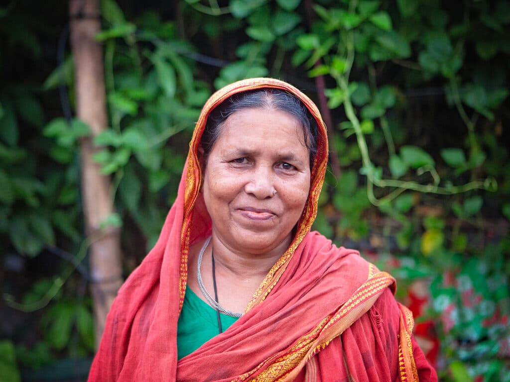 Foto: Diakonia En kvinna i söd sari ler mot kameran, i bakgrunden är ett grönt buskage.