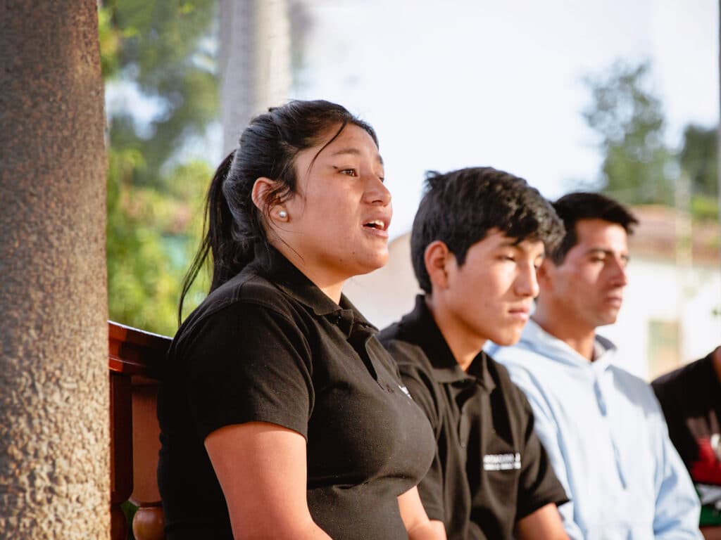 En ung kvinna och tre unga män sitter på en bänk bredvid en pelare av sten.