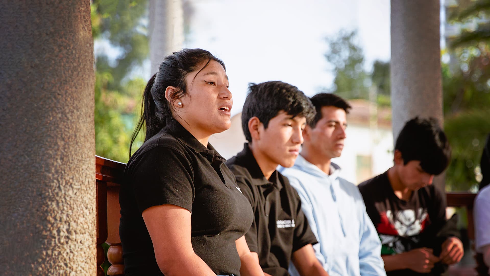 Foto: Siara Horna En ung kvinna och tre unga män sitter på en bänk bredvid en pelare av sten.
