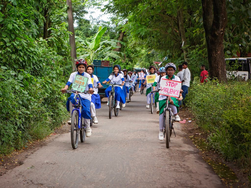 En grupp flickor i skoluniform cyklar tillsammans med plakat på cyklarna.