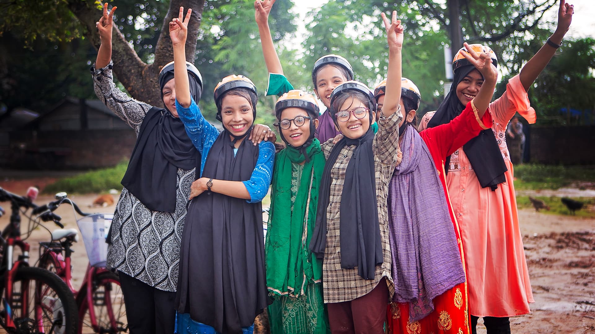 En grupp flickor med cykelhjälmar står och håller upp händerna i luften och ser in i kameran.