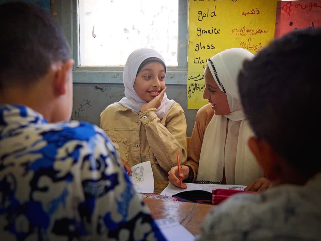 Foto: Sima Diab Två flickor med vita hijabs sitter i ett klassrum och pratar med varandra.