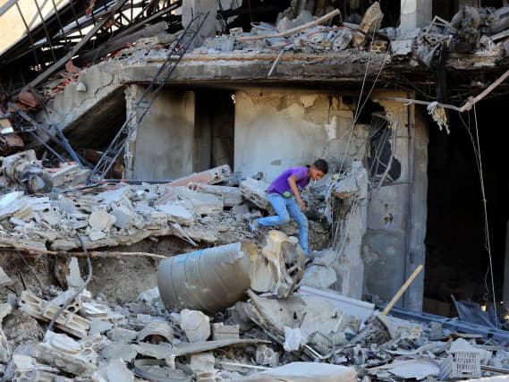 Foto: ACT Alliance Byggnader i ruiner och rasmassor, och en ung man som springer bland bråtet.