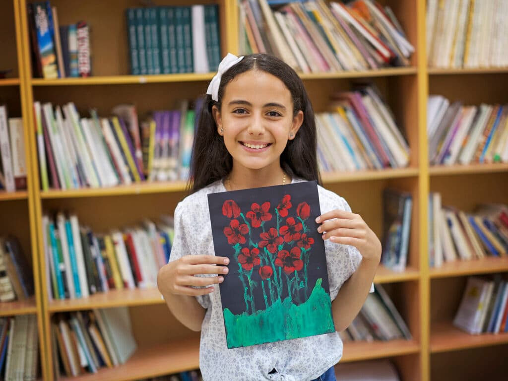 Foto: Ahmad Daghlas En flicka med långt mörkt hår håller upp en teckning föreställande röda blommor.