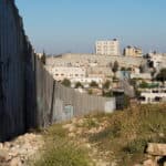 A high concrete wall runs through a valley, with houses next to the wall.