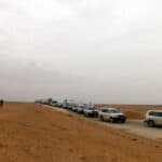A convoy of cars with United Nations flags driving through dry land.
