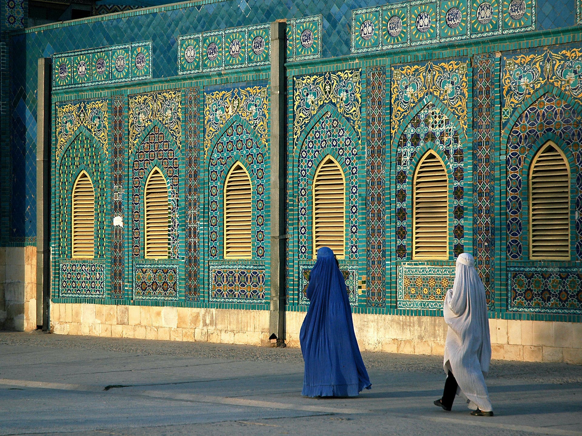 Two women walk in front of a mosque.